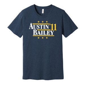 May include: A navy blue t-shirt with a white graphic that says "Austin'11 Bailey" in a retro font. The graphic is surrounded by yellow stars.