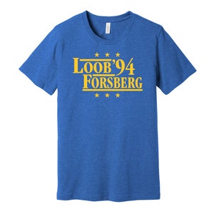 Puede incluir: Una camiseta azul real con un gráfico dorado que dice "Loob'94 Forsberg" con cinco estrellas doradas arriba y abajo del texto.