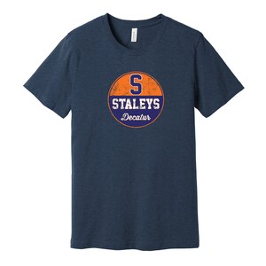 May include: A navy blue t-shirt with a vintage-style circular logo featuring an orange background, a blue "S" and the text "Staleys Decatur".