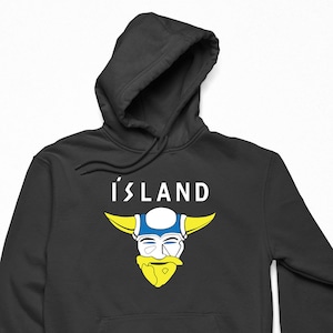 Puede incluir: Sudadera con capucha negra con un gráfico blanco de un vikingo con un casco azul y amarillo y la palabra "Islandia" en blanco.