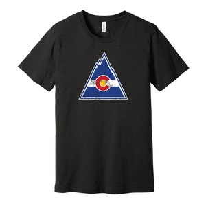 May include: Black t-shirt with a distressed white triangle graphic featuring the Colorado state flag. The flag is blue, white, and red with a large yellow circle in the center.