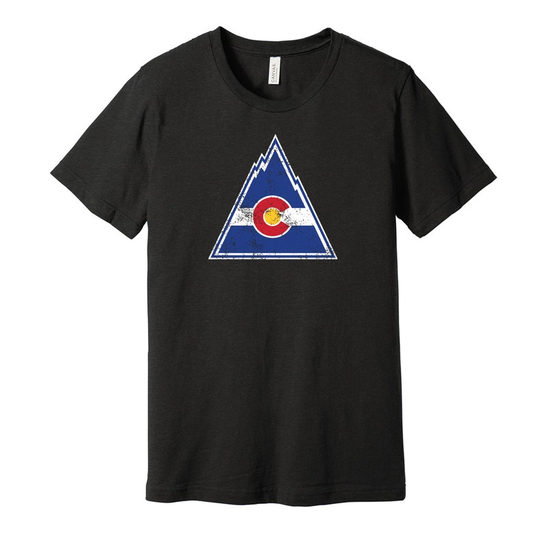May include: Black t-shirt with a distressed white triangle graphic featuring the Colorado state flag. The flag is blue, white, and red with a large yellow circle in the center.