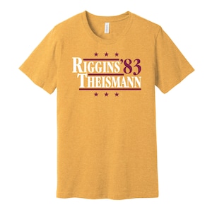 May include: A yellow t-shirt with a burgundy print that reads "Riggins '83 Theisman" with stars above and below the text.