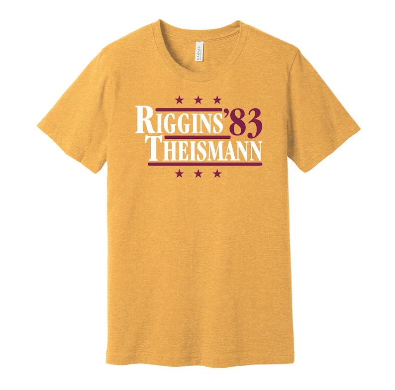 May include: A yellow t-shirt with a burgundy print that reads "Riggins '83 Theisman" with stars above and below the text.
