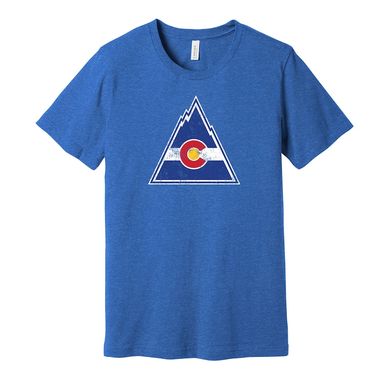 May include: A royal blue t-shirt with a distressed white triangle graphic featuring the Colorado state flag. The flag is blue, white, and red with a large yellow circle in the center.
