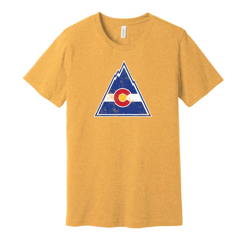 May include: A yellow t-shirt with a distressed graphic of a mountain range and the Colorado state flag. The flag is blue, white, and red with a large "C" in the center.
