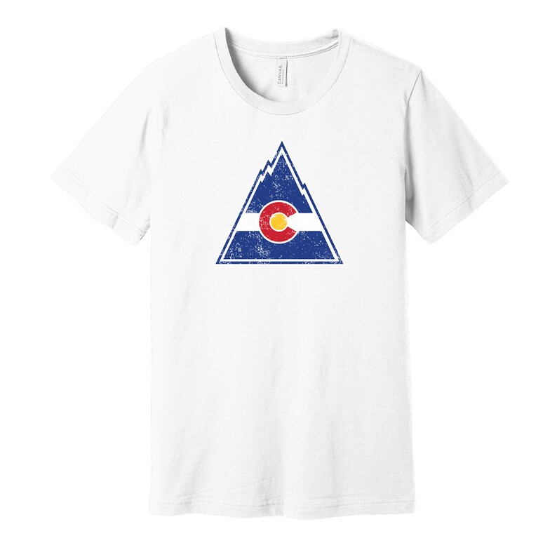 May include: White t-shirt with a distressed graphic of a mountain range with the Colorado flag inside. The flag is red, yellow, and blue with a large "C" in the center.