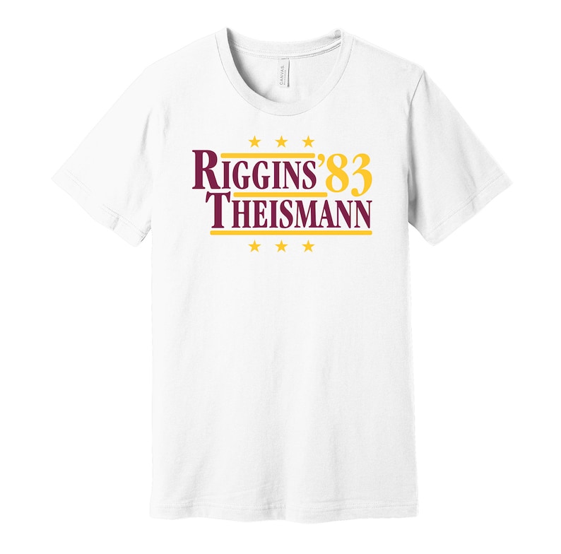 May include: White t-shirt with a burgundy and gold graphic that reads "Riggins '83 Theisman" with five gold stars above and below the text.
