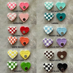 May include: A selection of heart-shaped magnets in a variety of colours and patterns. Some feature a checkerboard design, while others are solid. Each magnet has the text "COURT SPOT" and a small, round magnet on the back. Colours include pink, blue, green, and brown.