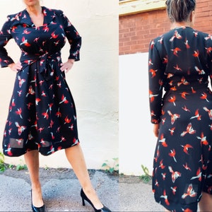 Puede incluir: Un vestido negro de envoltura con estampado de p&aacute;jaros rojos y azules. El vestido tiene manga larga y un lazo en la cintura.
