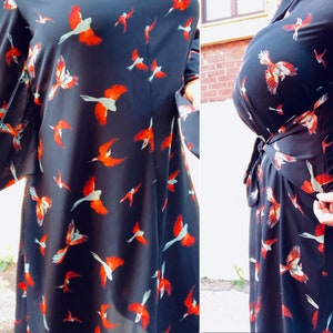 Puede incluir: Un vestido negro de envoltura con estampado de p&aacute;jaros rojos y blancos. El vestido tiene mangas largas y un lazo en la cintura.