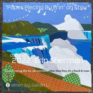 以下が含まれることがあります： 青い空、白い鳥、緑の丘、青い川に流れ落ちる滝の風景が描かれた布製のキルト。テキストには「Paper Piecing By Erin on Etsy」、「copyright 2022 Erin Sherman」、「sewn by Sarah L.」と記されています。