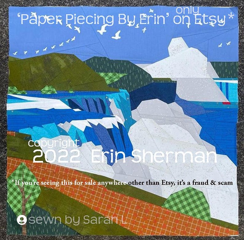 以下が含まれることがあります： 青い空、白い鳥、緑の丘、青い川に流れ落ちる滝の風景が描かれた布製のキルト。テキストには「Paper Piecing By Erin on Etsy」、「copyright 2022 Erin Sherman」、「sewn by Sarah L.」と記されています。