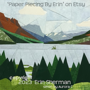 Può includere: Un blocco di trapunta in tessuto raffigurante un paesaggio con pini verde scuro in primo piano, un lago azzurro e montagne marroni e blu sotto un cielo pallido. Il testo recita 'Paper Piecing By Erin' on Etsy e copyright 2023 Erin Sherman.