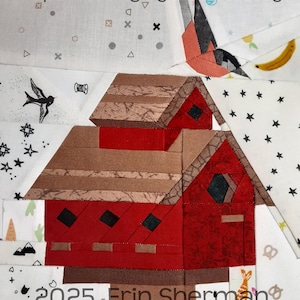 May include: A red paper pieced barn with a brown roof and black windows. The barn is surrounded by a white background with various small paper pieced designs, including stars, birds, and a banana.