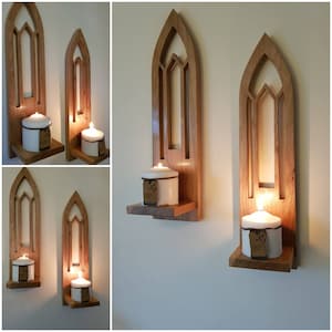 May include: Two wooden wall shelves with arched openings and a small shelf for candles. The shelves are stained a light brown colour and have a rustic look. Each shelf has a white candle on it.