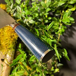 May include: A close-up of a blue and gold patterned knife handle with a silver band. The handle is made of a durable material and has a sleek, modern design.