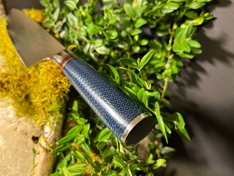 May include: A close-up of a blue and gold patterned knife handle with a silver band. The handle is made of a durable material and has a sleek, modern design.