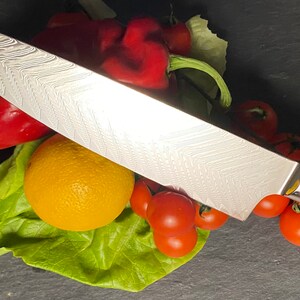 May include: A silver chef's knife with a blue and gold handle, resting on a bed of lettuce, tomatoes, and red peppers.