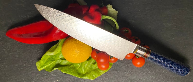 May include: A silver chef's knife with a blue and gold handle, resting on a bed of lettuce, tomatoes, and red peppers.