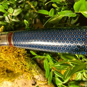 May include: Close-up of a blue and silver kitchen knife with a honeycomb pattern on the handle. The handle has a red and gold accent.