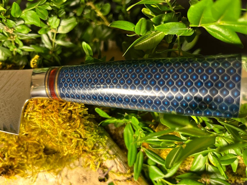 May include: Close-up of a blue and silver kitchen knife with a honeycomb pattern on the handle. The handle has a red and gold accent.