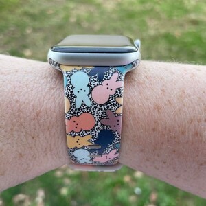 May include: A silver Apple Watch with a colourful patterned band featuring cartoon bunnies and a leopard print background.
