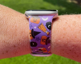 Puede incluir: Una banda de Apple Watch morada con un estampado de temática de Halloween que presenta calabazas, sombreros de bruja, estrellas y lunas.