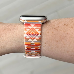 May include: A silver Apple Watch with a white and orange geometric patterned band.
