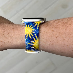 May include: A white Apple Watch with a blue and yellow tie-dye patterned band.