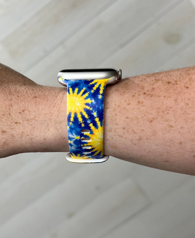 May include: A white Apple Watch with a blue and yellow tie-dye patterned band.