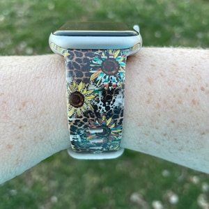 May include: A silver Apple Watch with a colorful band featuring a leopard print and sunflowers. The band is made of silicone and has a secure clasp.