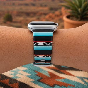 May include: A silicone smartwatch band featuring a horizontal pattern of turquoise, black, white, and thin red stripes. The design includes geometric diamond shapes and repeating linear motifs across the flexible strap, which is attached to a silver watch case.