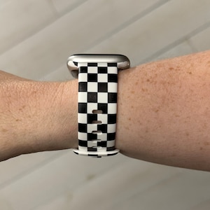 May include: A black and white checkered watch band. The band is made of a soft, flexible material and has a classic checkered pattern.