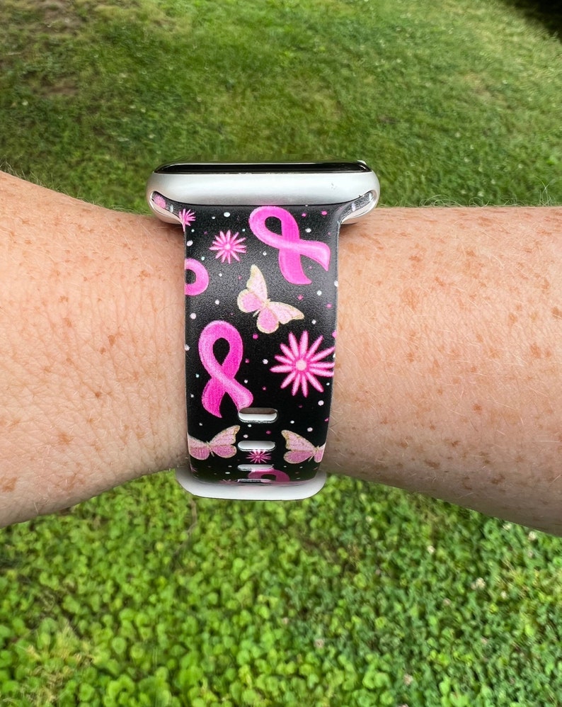 May include: A black and white watch strap with pink ribbon and butterfly designs. The strap is made of silicone and is compatible with Apple Watch.