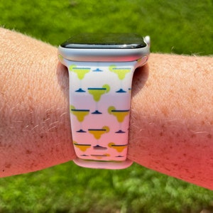 May include: A white Apple Watch with a yellow and blue patterned band featuring a repeating design of a cartoon castle. The watch face is black.