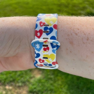 May include: A white silicone watch band with a pattern of red, blue, and yellow puzzle pieces and hearts.