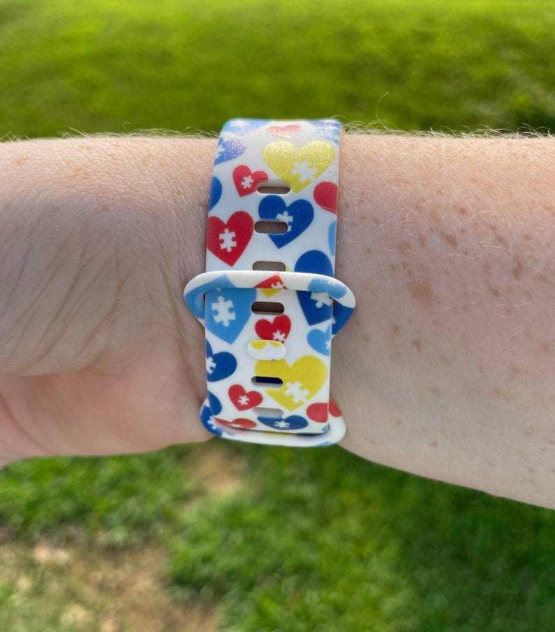 May include: A white silicone watch band with a pattern of red, blue, and yellow puzzle pieces and hearts.