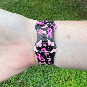 May include: A black watch strap with a pink ribbon and butterfly pattern. The strap is made of silicone and is compatible with most smartwatches.