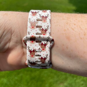 May include: White silicone watch band with a repeating pattern of red-nosed reindeer with red bows.