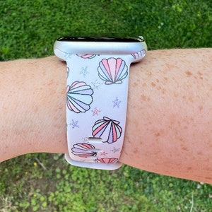 May include: White Apple Watch band with a seashell and starfish pattern. The band is made of silicone and has a white background with pink, purple, and blue seashells and starfish.