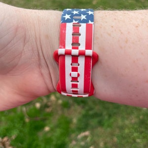 May include: A red, white, and blue watch band with a stars and stripes pattern. The band is made of a soft, flexible material and has a buckle closure.