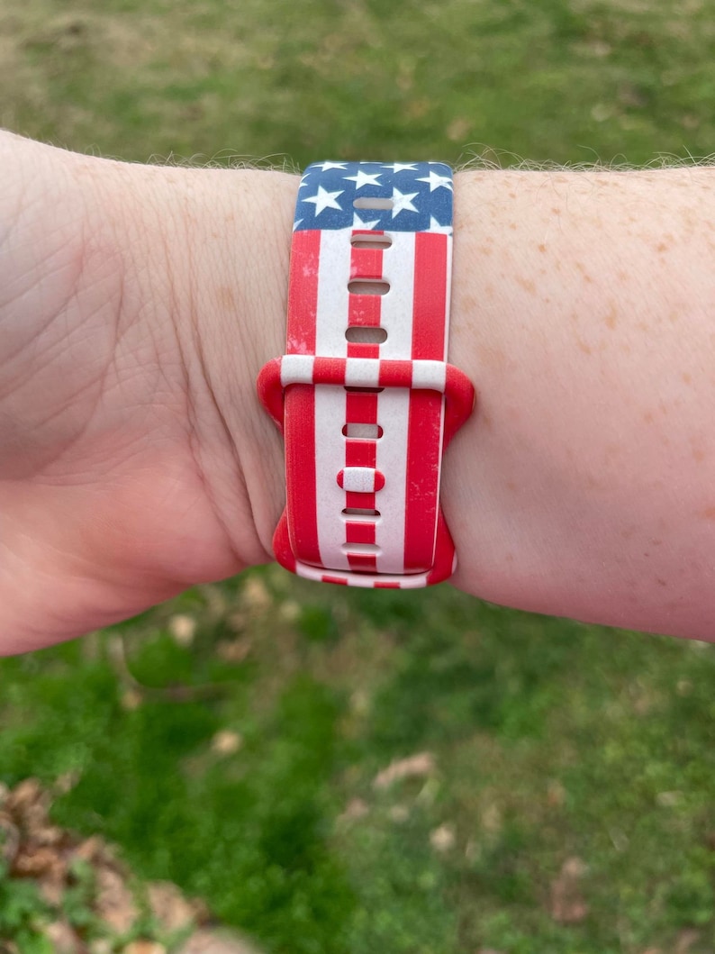 May include: A red, white, and blue watch band with a stars and stripes pattern. The band is made of a soft, flexible material and has a buckle closure.