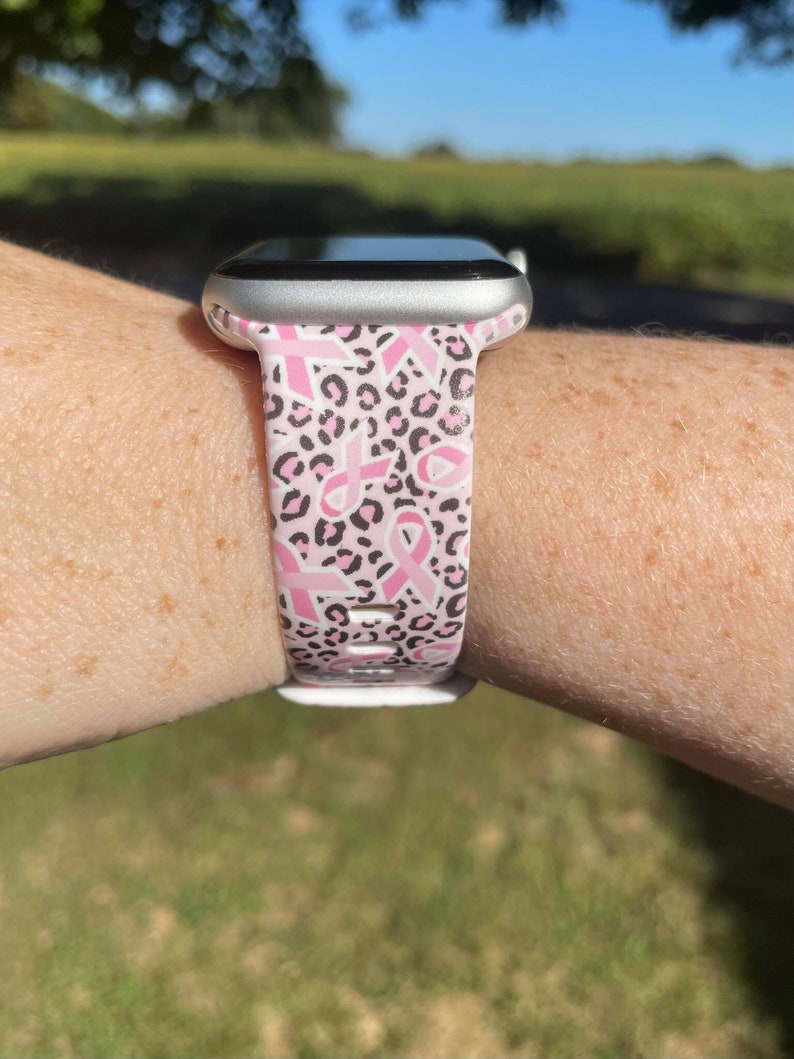 May include: A pink and black leopard print Apple Watch band with pink ribbon designs.