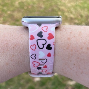 May include: A pink Apple Watch band with a pattern of red, black, and white hearts.