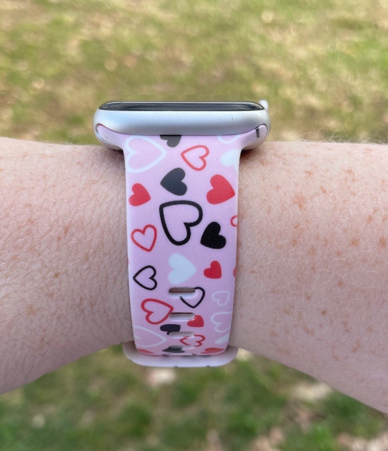 May include: A pink Apple Watch band with a pattern of red, black, and white hearts.