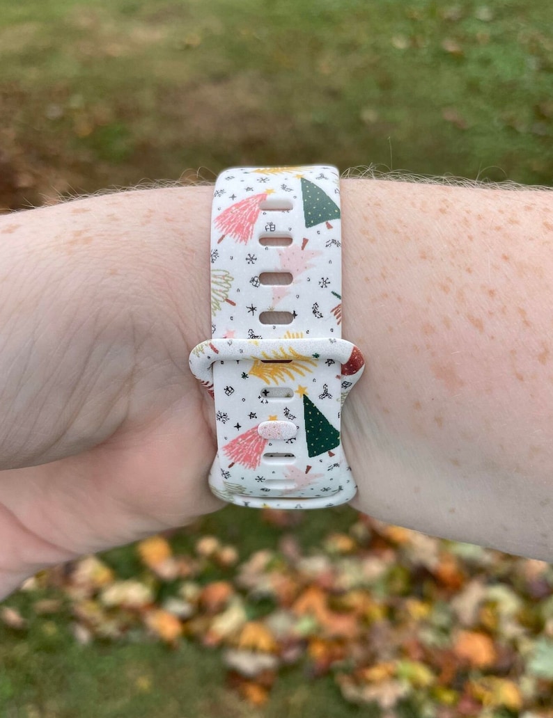 May include: White watch strap with a Christmas tree pattern. The strap has a white background with green, red, pink, and yellow Christmas trees, stars, and other festive designs.