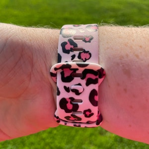 Puede incluir: Una correa de reloj de estampado de leopardo rosa y negro con una hebilla negra.
