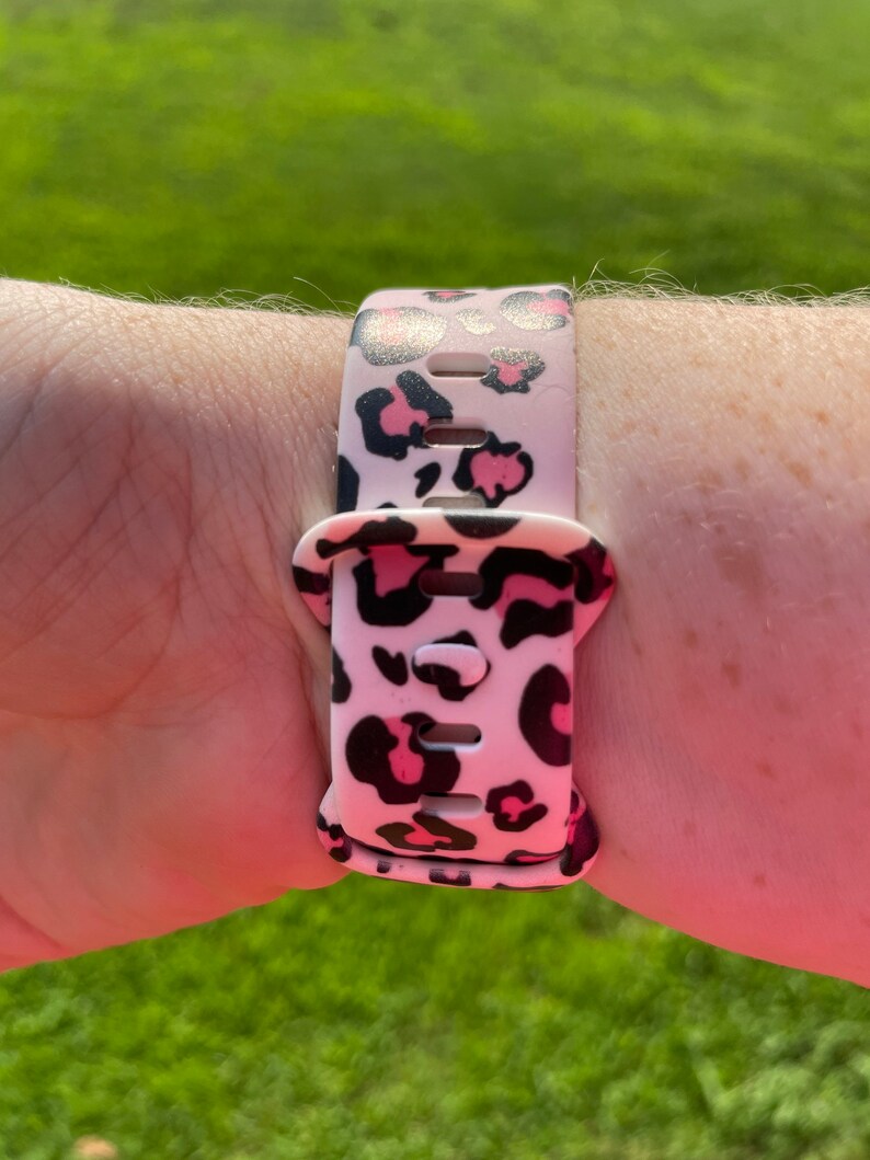 Puede incluir: Una correa de reloj de estampado de leopardo rosa y negro con una hebilla negra.