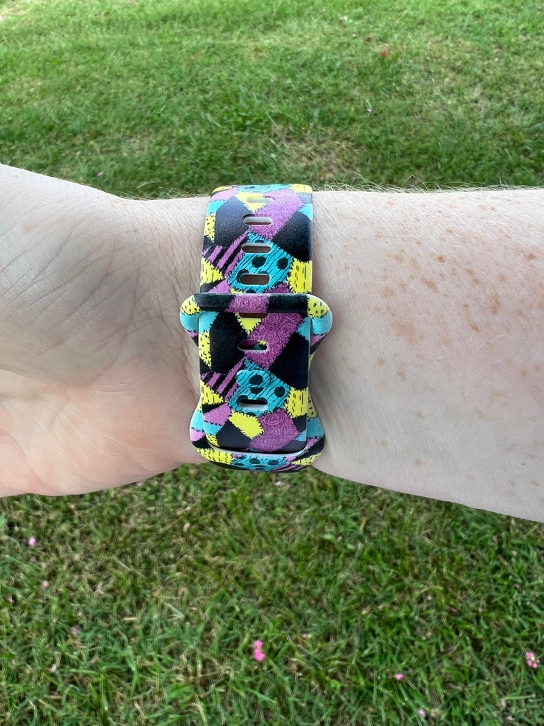 May include: A colorful watch band with a patchwork design featuring black, yellow, pink, and blue colors. The band is made of silicone and has a buckle closure.